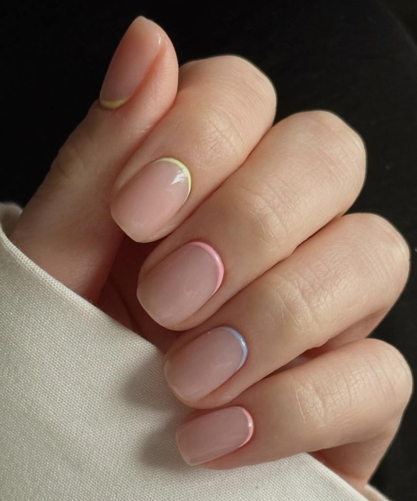 Close-up of nails with rainbow-colored reverse French tips on a beige base.